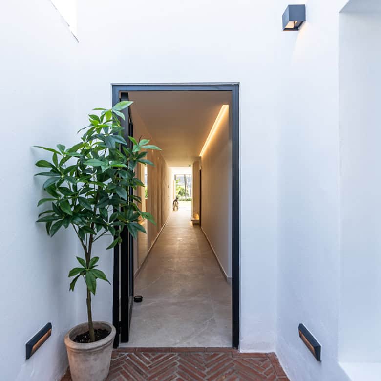 Modern Marbella townhouse entrance with white walls, potted plant, and sleek hallway leading inside.