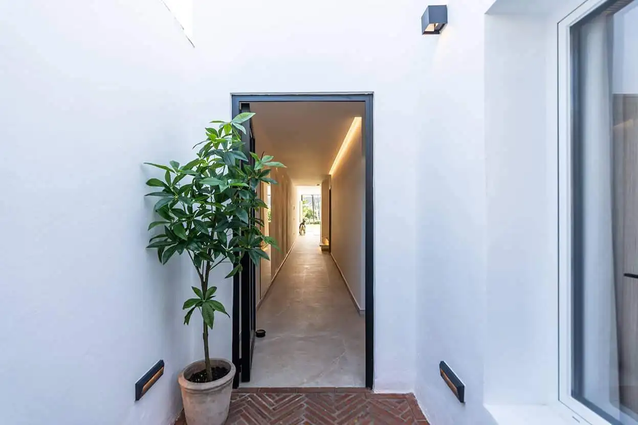 Modern Marbella townhouse entrance with white walls, potted plant, and sleek hallway leading inside.