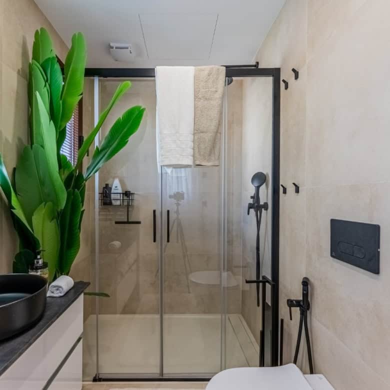 Bright, contemporary bathroom featuring a large green plant, sleek black fixtures, and a spacious gl.