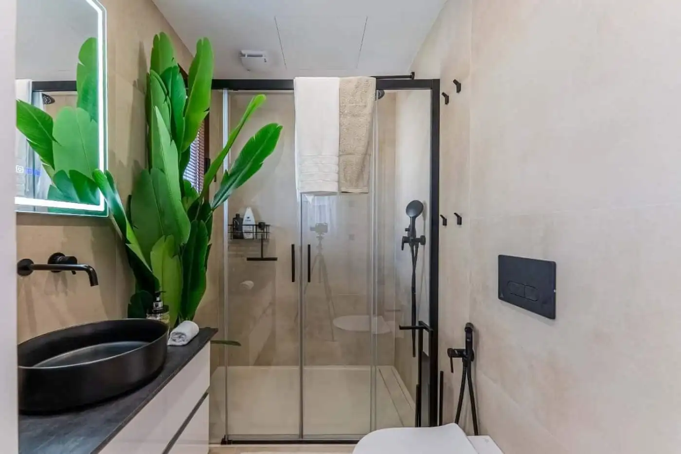 Bright, contemporary bathroom featuring a large green plant, sleek black fixtures, and a spacious gl.
