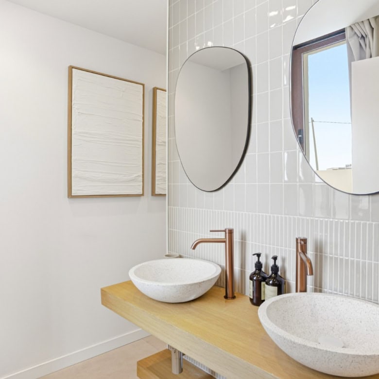 Bathroom with dual vessel sinks, round mirrors, and minimalist decor.