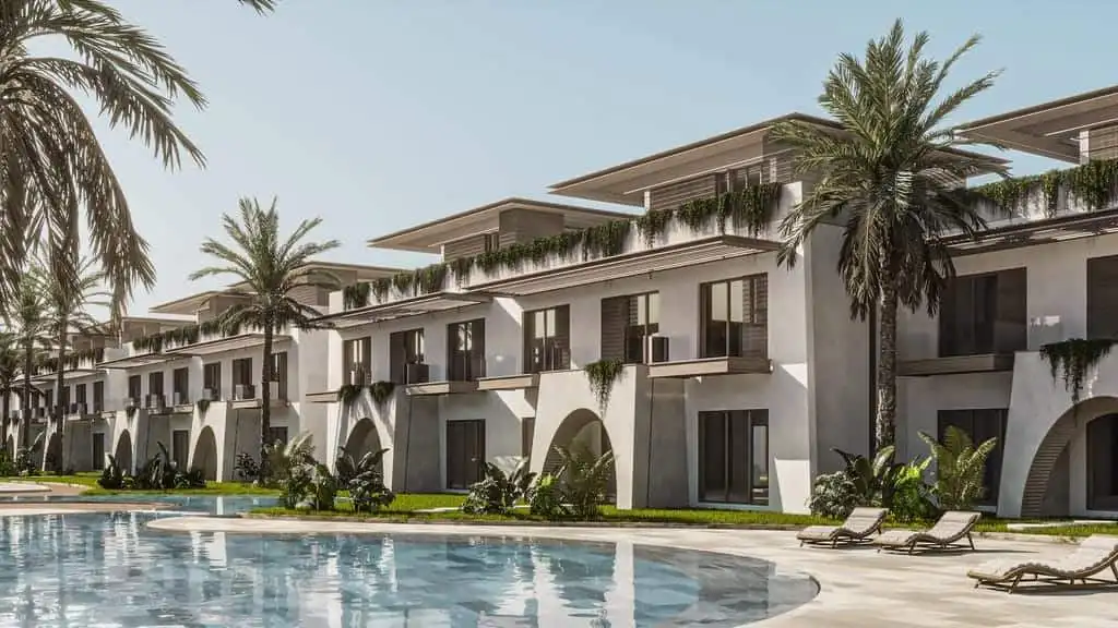 Modern beachfront apartment complex with pool and palm trees.