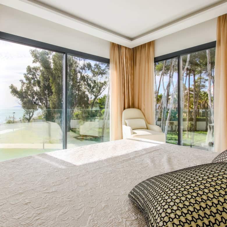 Beachfront bedroom with large windows overlooking the sea and lush greenery.