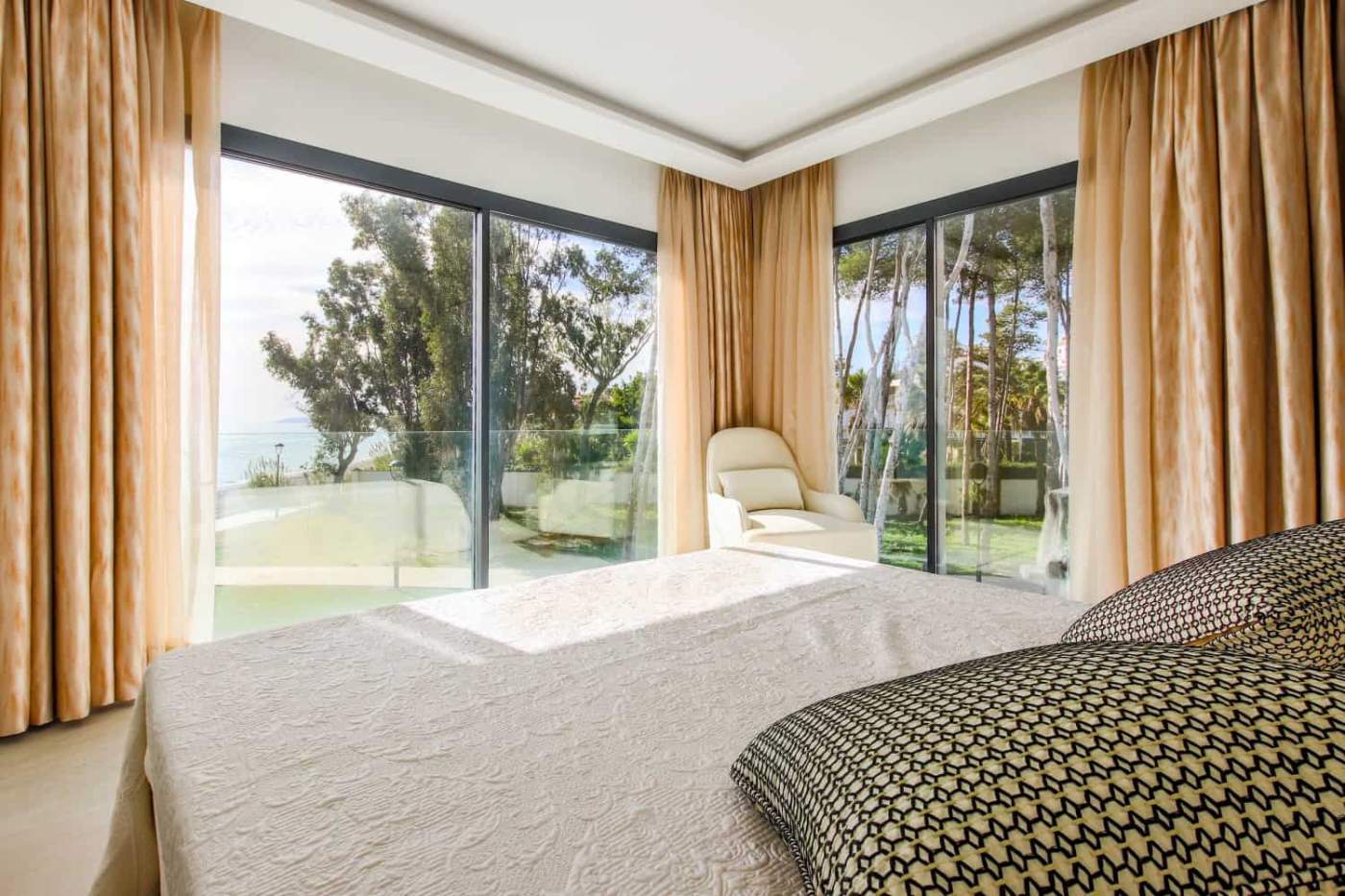 Beachfront bedroom with large windows overlooking the sea and lush greenery.