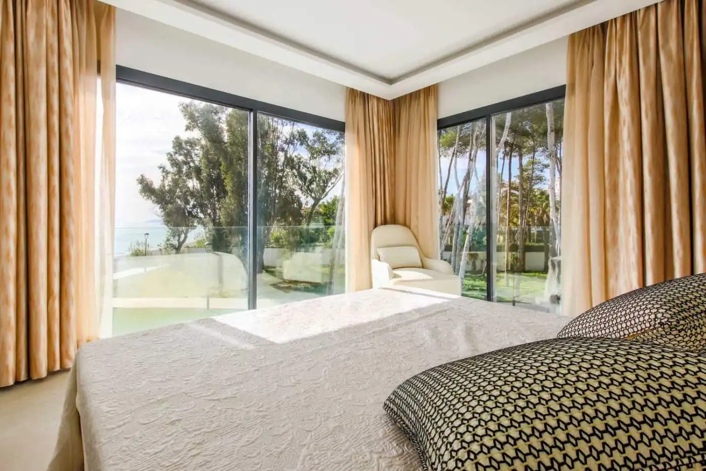 Beachfront bedroom with large windows overlooking the sea and lush greenery.