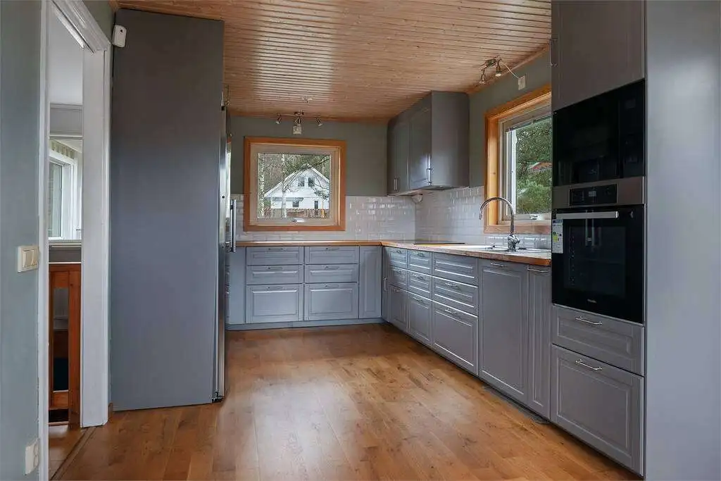 Spacious kitchen featuring wooden floors, ample cabinetry, and large windows offering natural light.