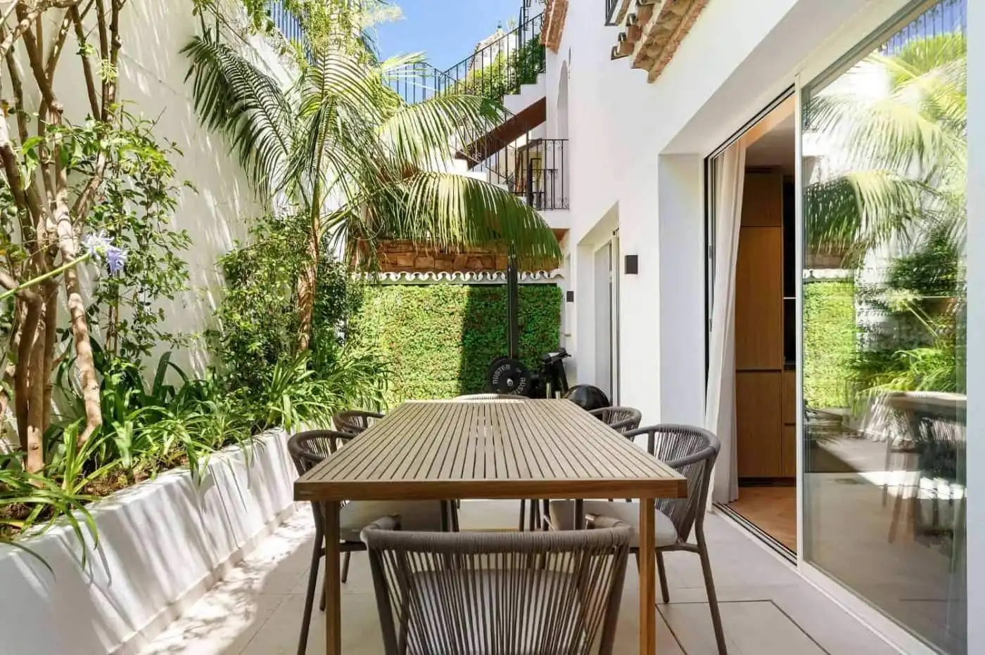 Modern Marbella townhouse terrace with outdoor dining area and lush greenery.