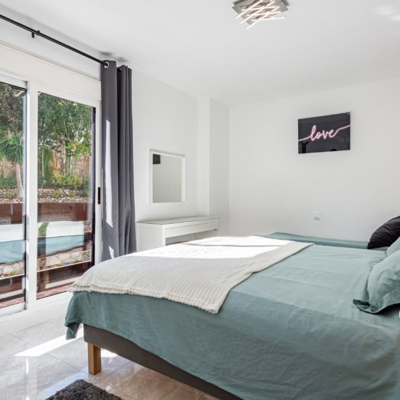 Spacious bedroom featuring large glass doors opening to a balcony, bright and airy interior.