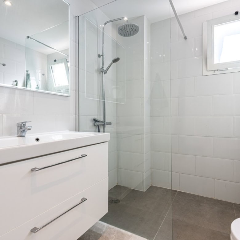 Bright and clean bathroom featuring a walk-in shower, white tiles, and a small window in La Maestran.