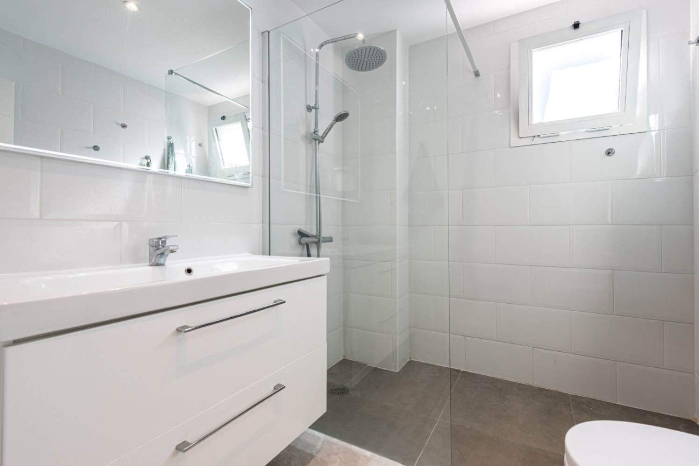 Bright and clean bathroom featuring a walk-in shower, white tiles, and a small window in La Maestran.