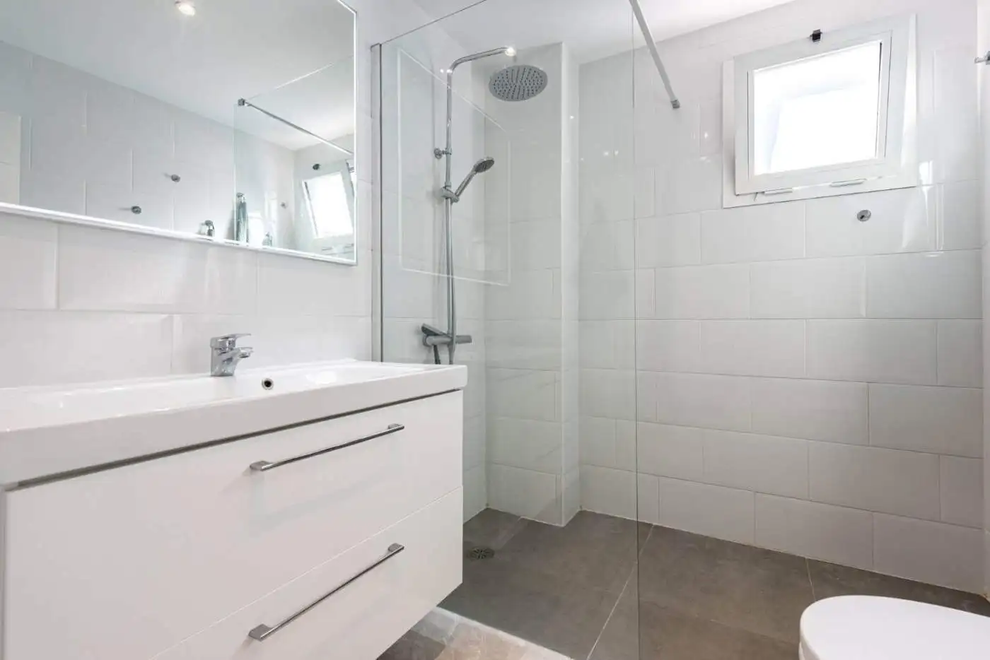 Bright and clean bathroom featuring a walk-in shower, white tiles, and a small window in La Maestran.