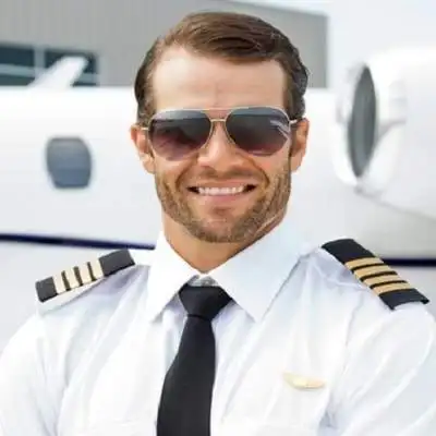 Pilot in uniform smiling with sunglasses in front of private jet.