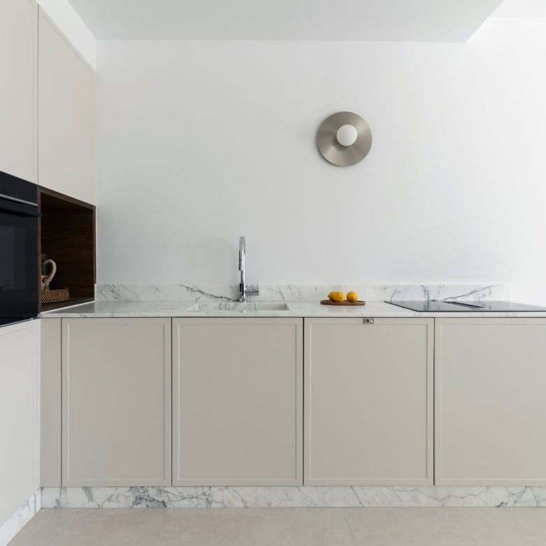Modern minimalist kitchen with white cabinets and marble countertops.