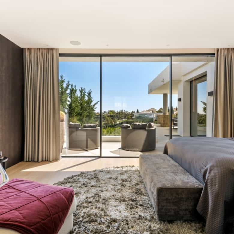 Elegant modern villa interior with spacious bedroom and balcony overlooking scenic surroundings.