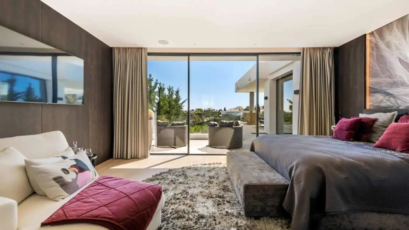 Elegant modern villa interior with spacious bedroom and balcony overlooking scenic surroundings.