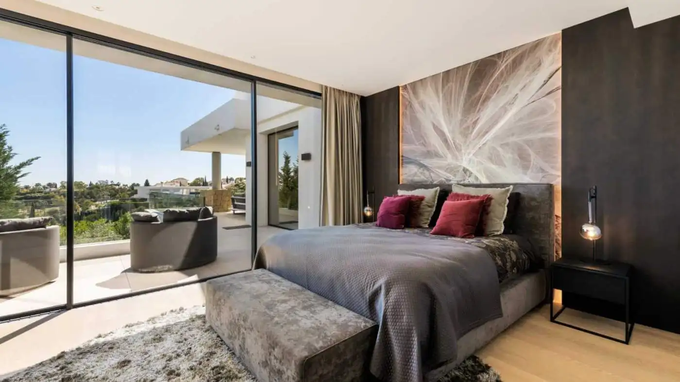 Elegant bedroom with large glass doors opening to a balcony in Los Flamingos Resort. Modern decor wi.