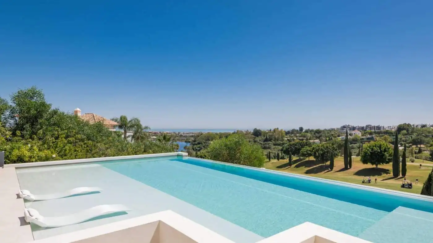 Modern infinity pool with lounge chairs and scenic golf course view in Los Flamingos Resort.