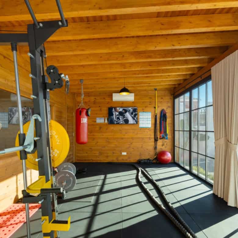 Home gym with wooden walls, large windows, and fitness equipment for a healthy lifestyle.