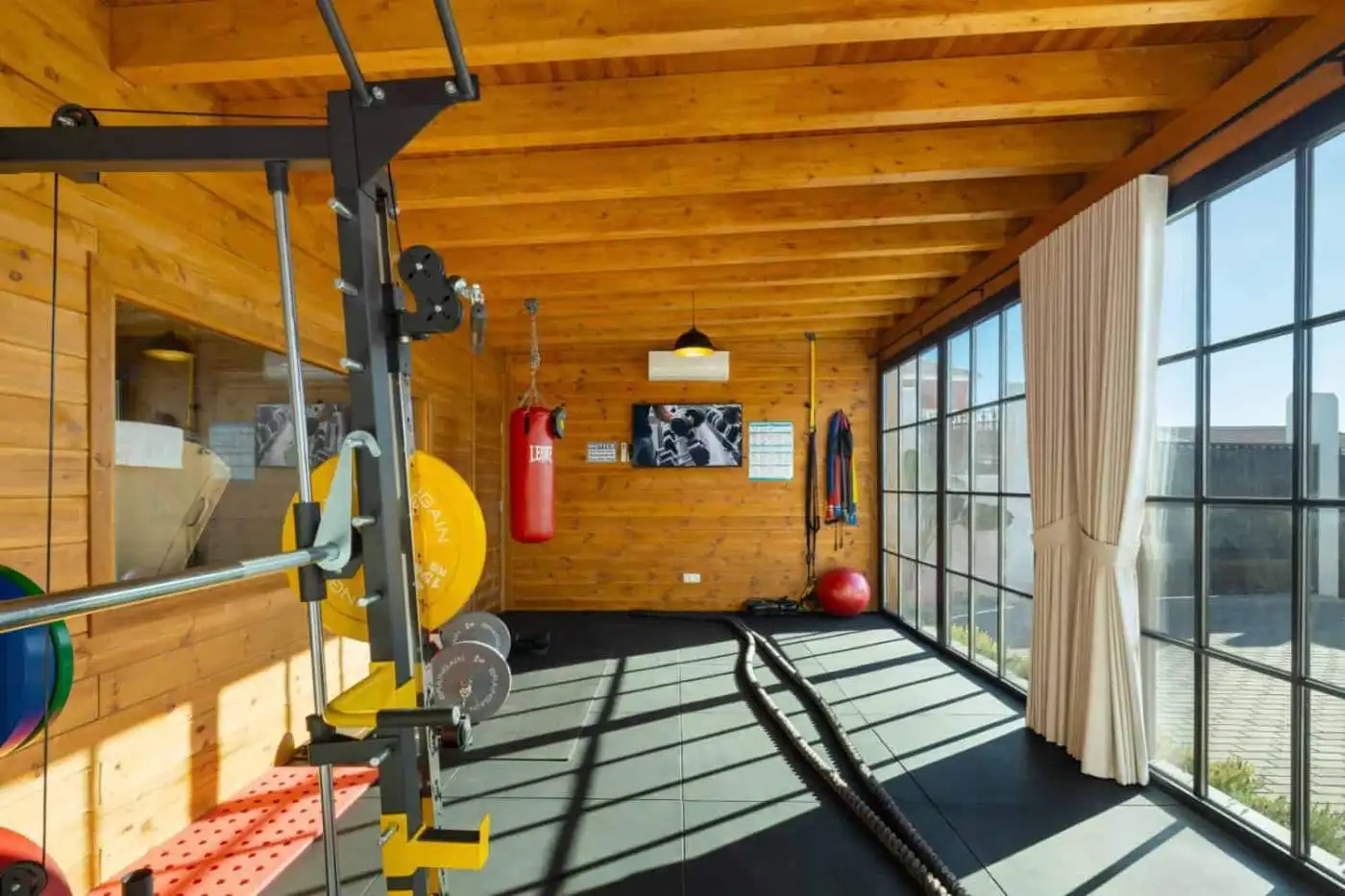 Home gym with wooden walls, large windows, and fitness equipment for a healthy lifestyle.