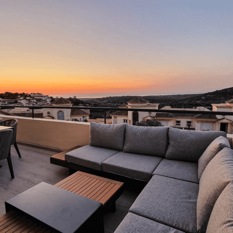 Modern penthouse terrace overlooking San Roque with panoramic sea views at sunset.
