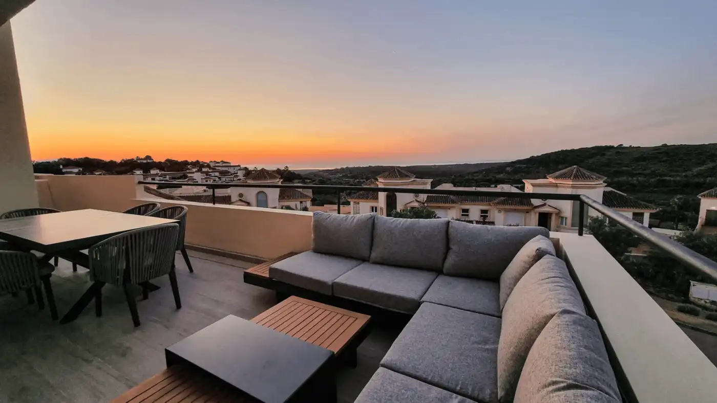Modern penthouse terrace overlooking San Roque with panoramic sea views at sunset.
