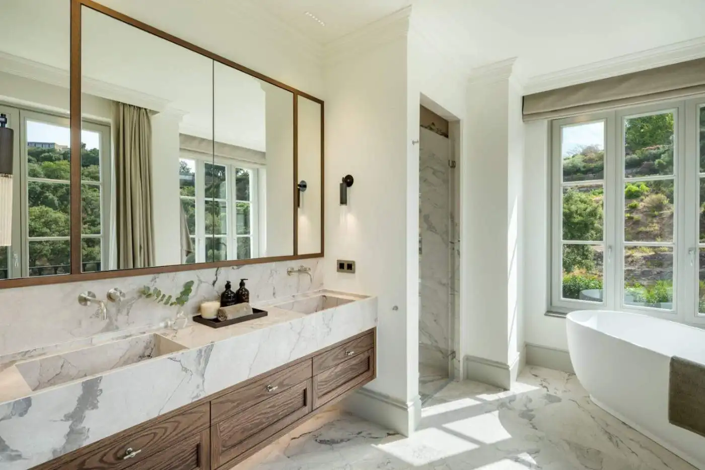 Elegant modern bathroom with marble finishes and large windows overlooking lush greenery.