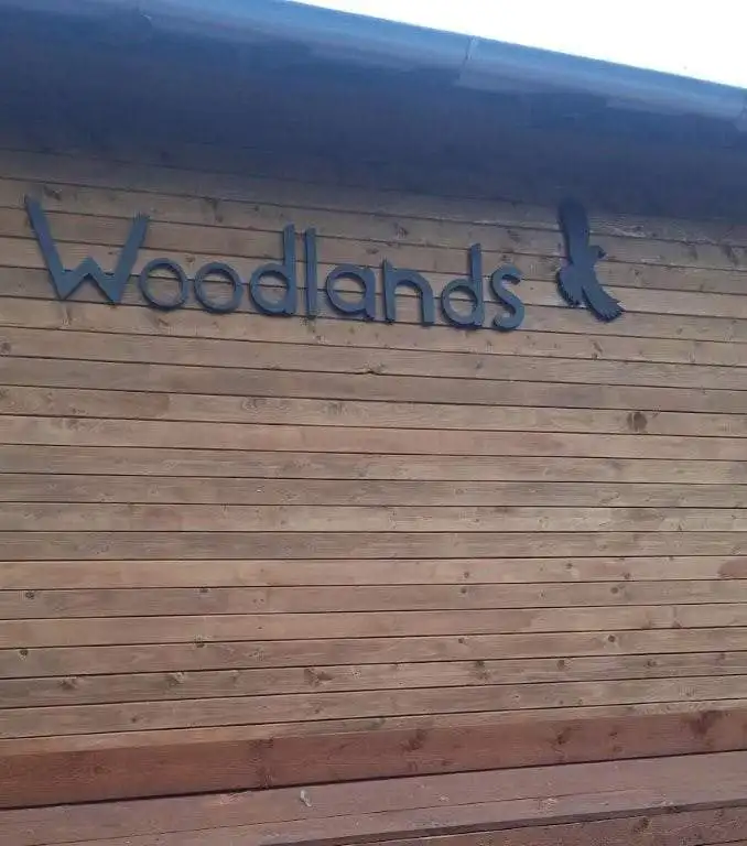 Woodlands sign on wooden building exterior in a natural setting.
