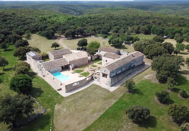 Elegant estate with historic stone buildings and a swimming pool in lush countryside.