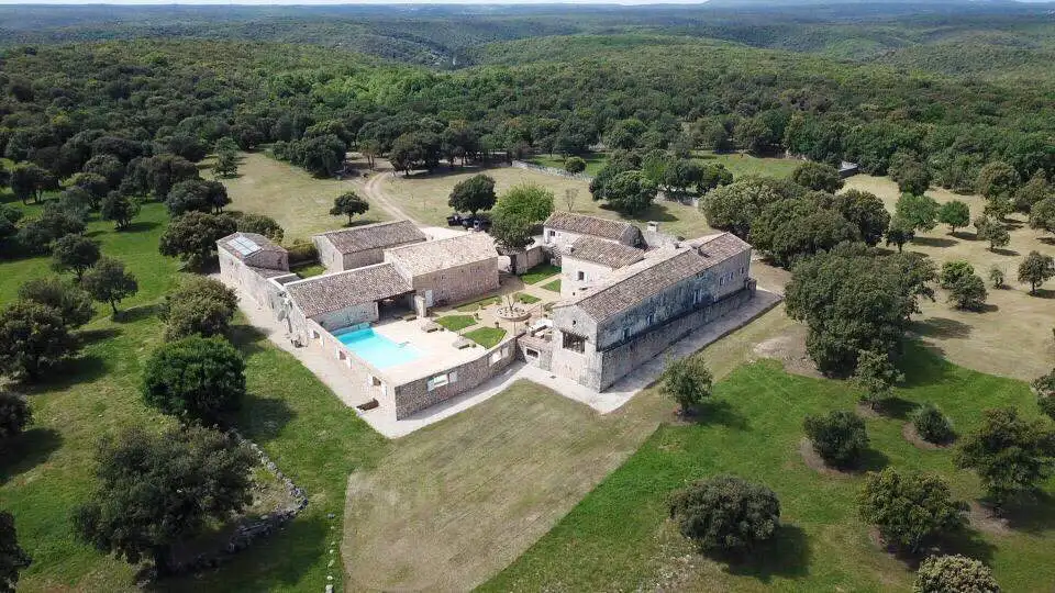 Elegant estate with historic stone buildings and a swimming pool in lush countryside.