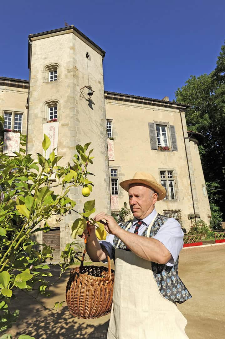 Château de la Chassaigne for Sale in Thiers France Château de la Chassaigne with a man harvesting fruit in the garden, historic French estate for sale.