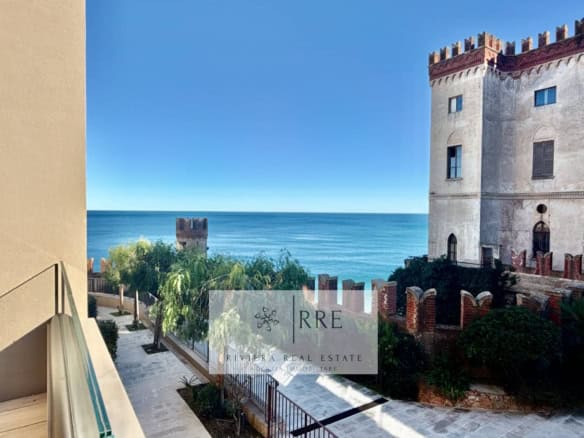 Historic castle overlooking the sea with lush greenery and clear blue sky.
