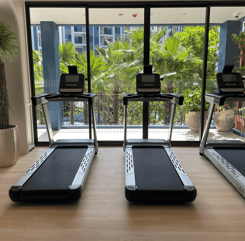 Modern gym with three treadmills and large glass windows overlooking lush greenery in Hua Hin.