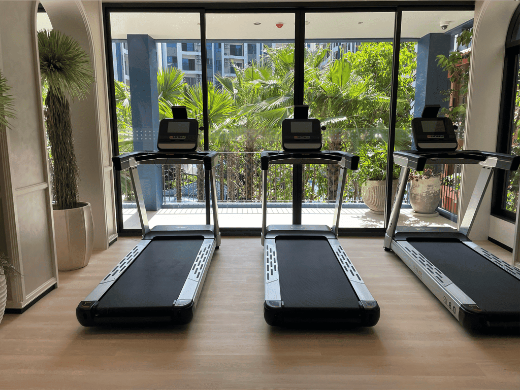 Modern gym with three treadmills and large glass windows overlooking lush greenery in Hua Hin.