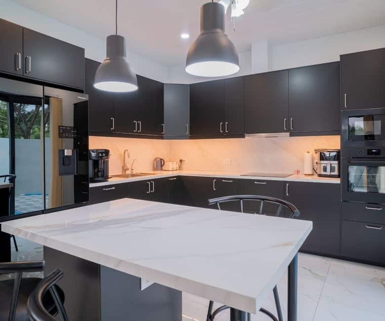 Modern black kitchen with sleek cabinetry and a central island for cooking and dining. Bright lighti.