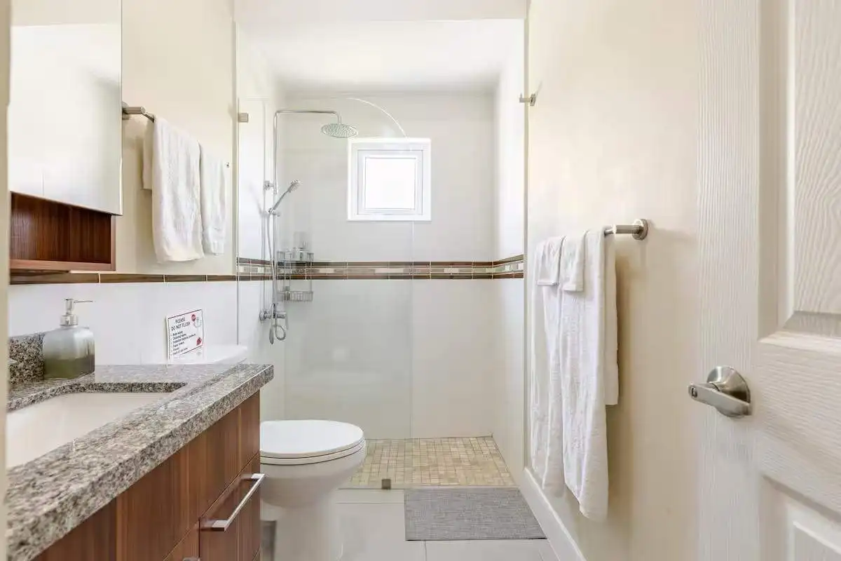 Luxury 3-Bed House in Sunshine Seashore Modern bathroom in luxury Jamaican seaside home with white tiles and wooden accents.