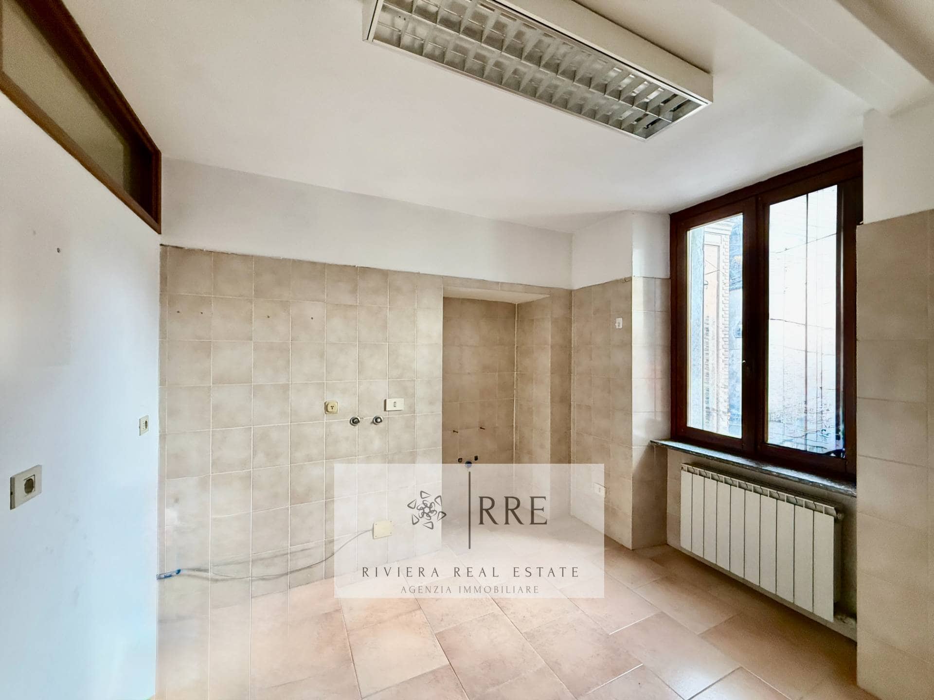 Modern kitchen with large window and beige tiled walls.