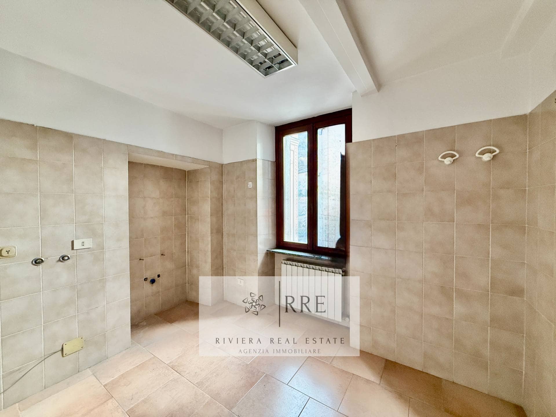 Spacious kitchen with natural light, beige tiles, and a large window overlooking the outside.