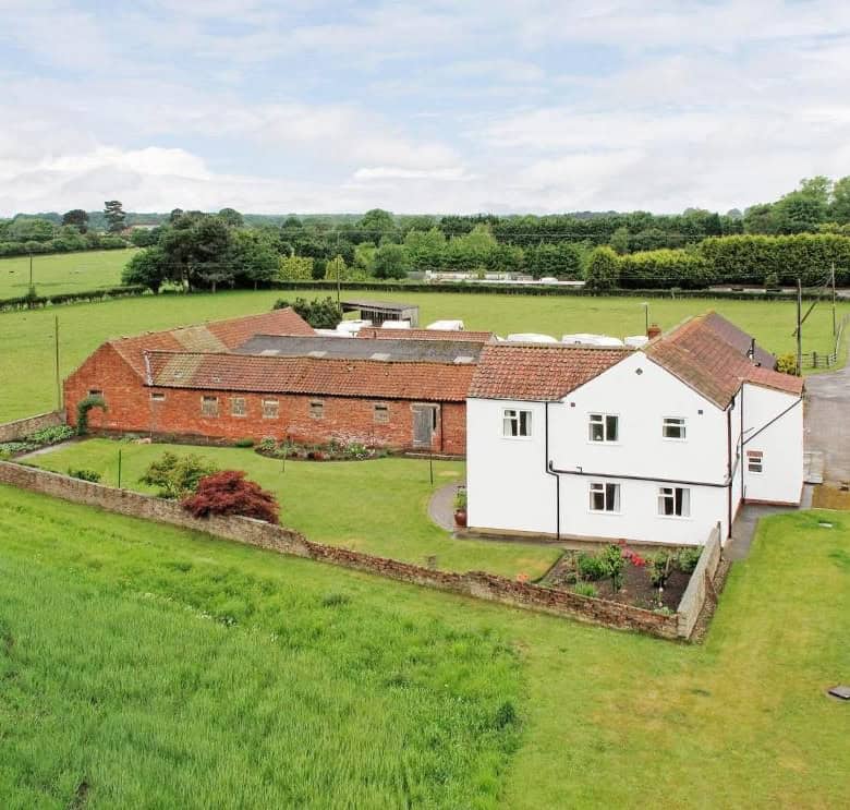 Country house with garden and surrounding green fields in a rural setting.