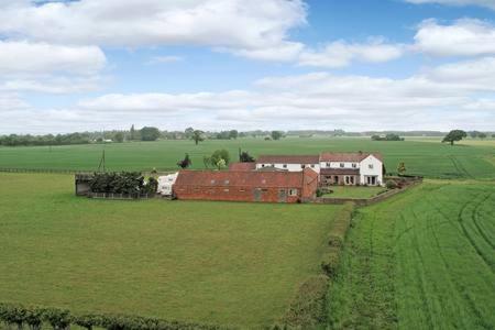 Farmhouse surrounded by lush green fields under a blue sky.