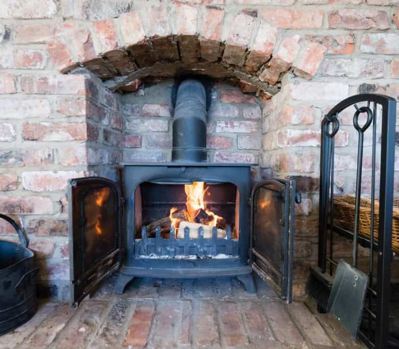 Fireplace with brick wall, black metal tools, and a wicker basket in a warm, inviting living space.