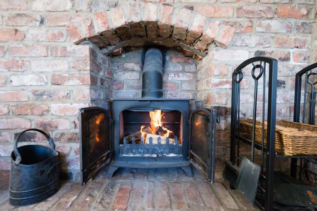Fireplace with brick wall and accessories in a cozy home setting Fireplace with brick wall, black metal tools, and a wicker basket in a warm, inviting living space.