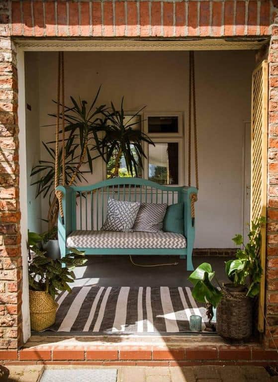 Outdoor porch swing with lush greenery and natural sunlight.