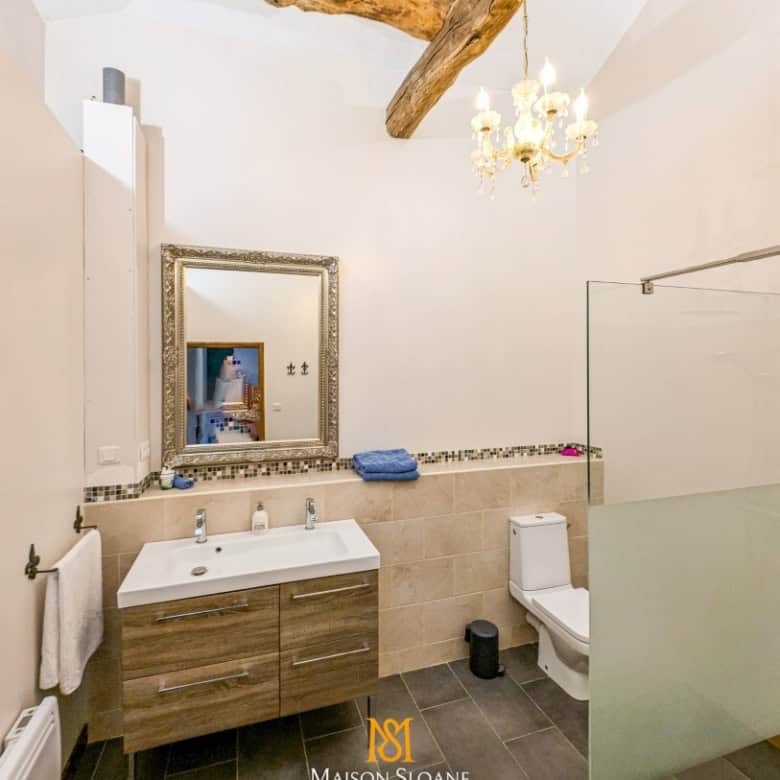 Spacious bathroom with modern fixtures, exposed wooden beams, and elegant decor in a luxury French c.