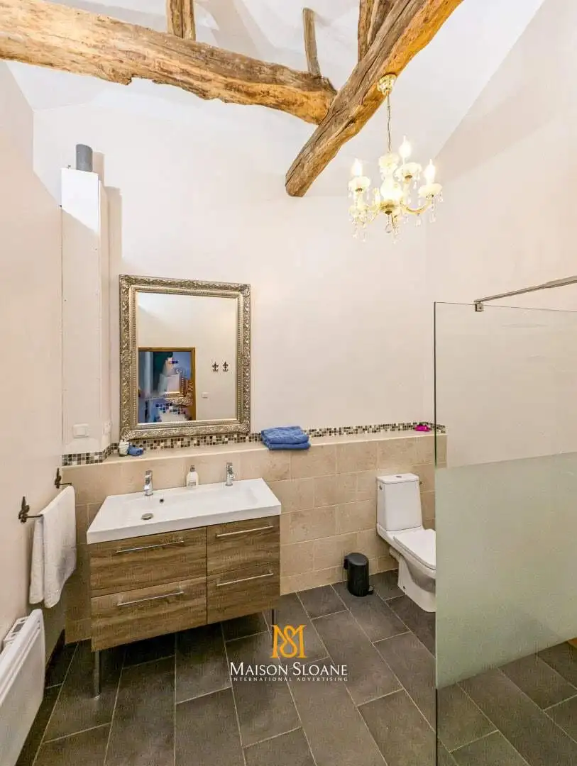 Spacious bathroom with modern fixtures, exposed wooden beams, and elegant decor in a luxury French c.