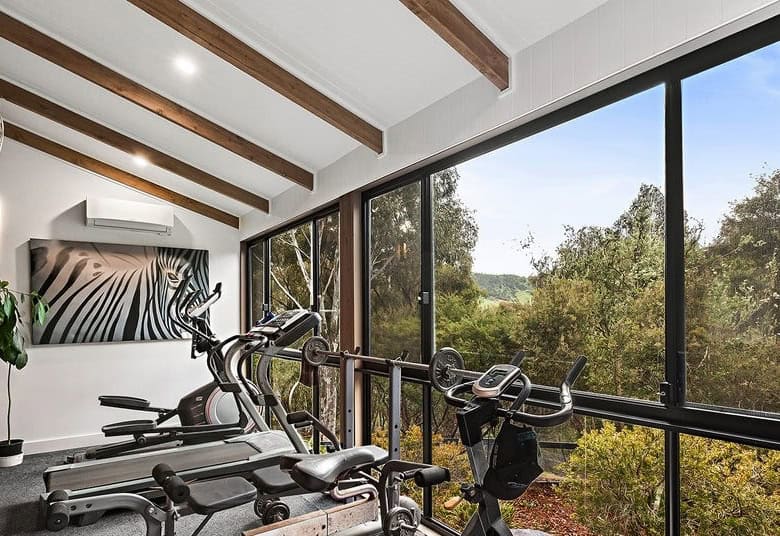 Modern indoor gym with large windows overlooking lush greenery in Flowerdale Vic.