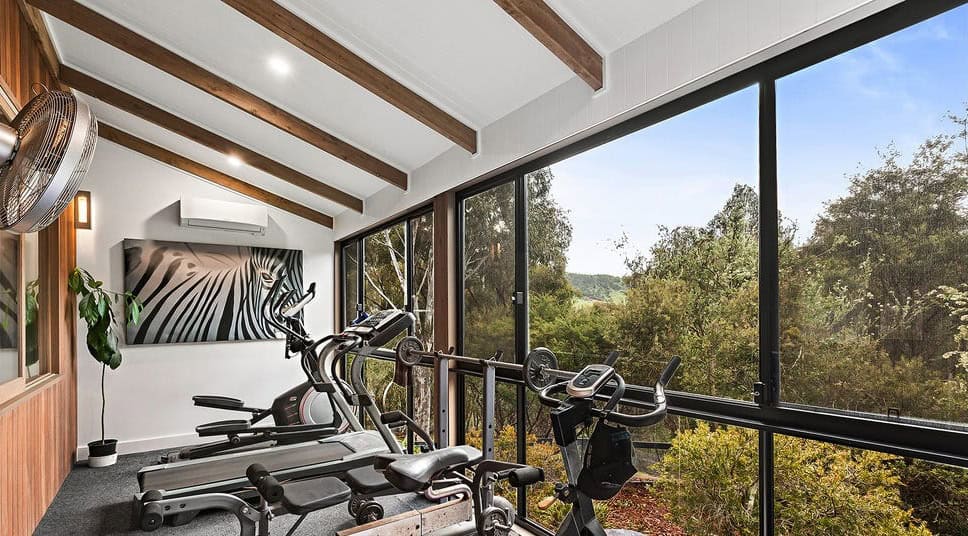 Modern indoor gym with large windows overlooking lush greenery in Flowerdale Vic.