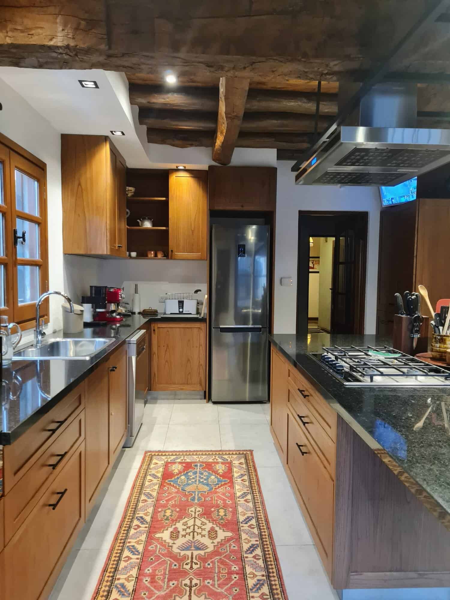 Cozy rustic kitchen with wooden cabinets and modern appliances Rustic kitchen featuring wooden cabinets, stainless steel appliances, and a colorful rug for a warm,.