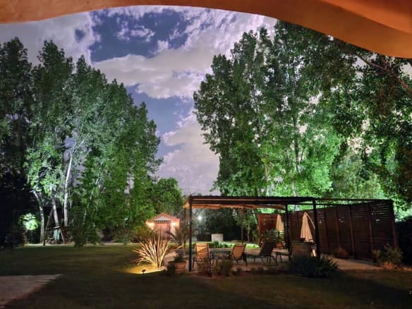 Beautiful backyard with tall trees, garden, and cozy outdoor seating at night.