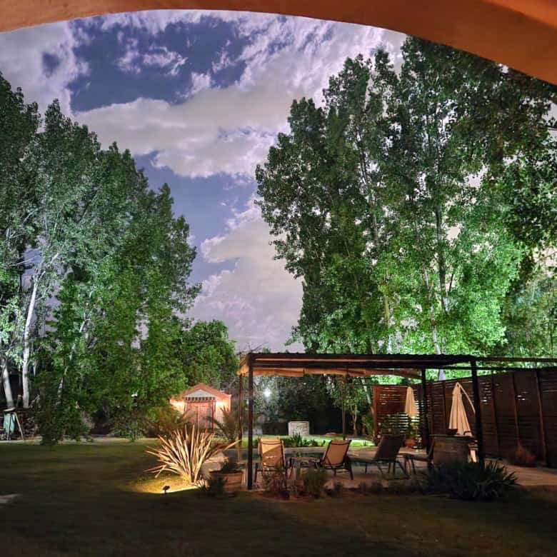 Beautiful backyard with tall trees, garden, and cozy outdoor seating at night.
