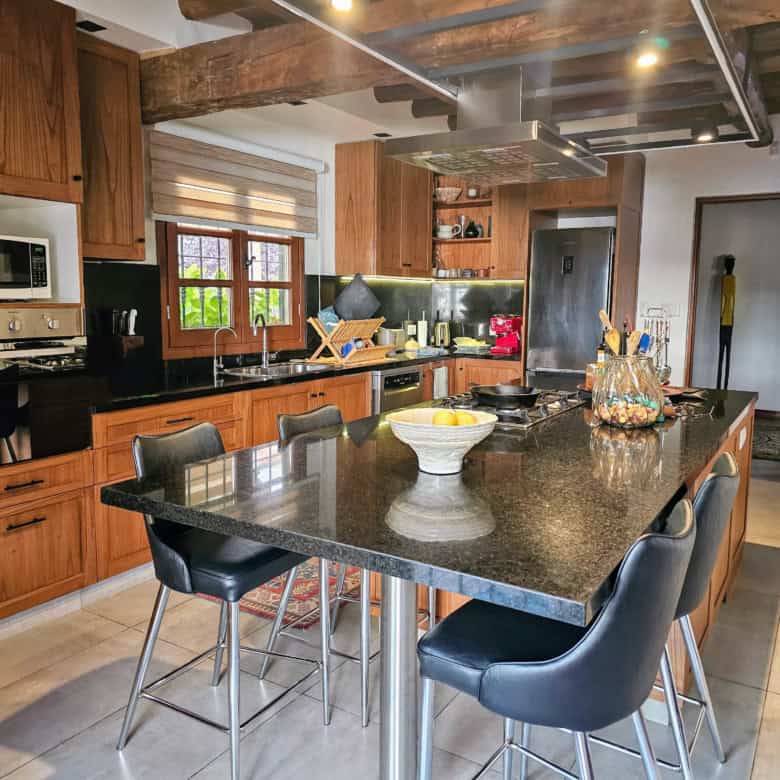 Modern wooden kitchen with island and black countertops, bright natural light, and contemporary appl.